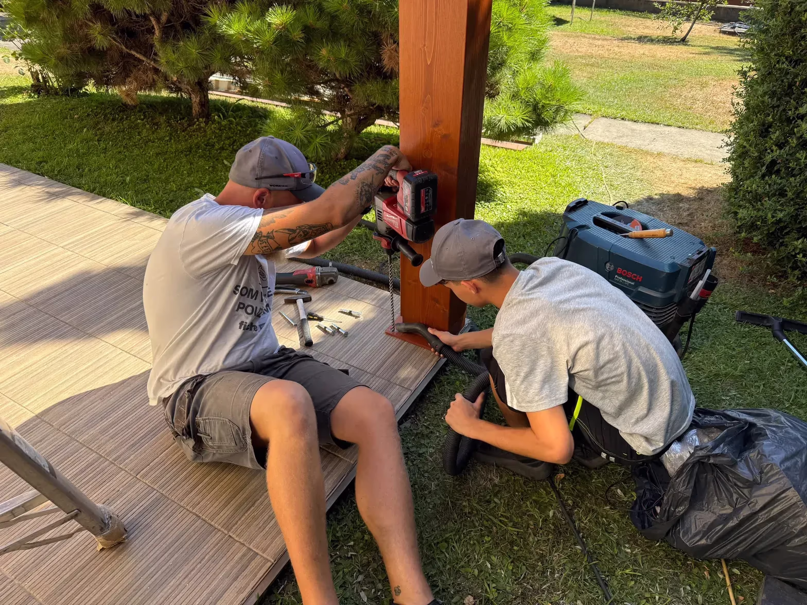 Installers drilling anchor holes into a wooden pergola's support post