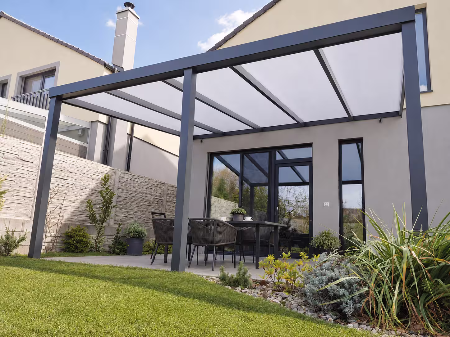 Anthracite Basic Class aluminium pergola with an opal roof beside a house with a chimney