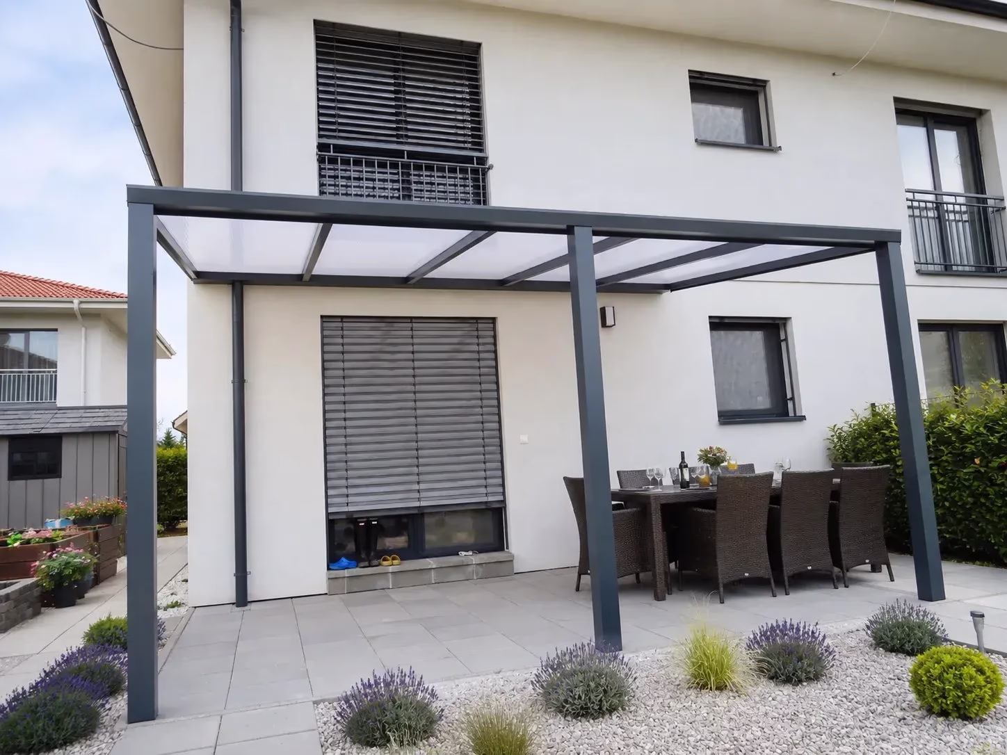Anthracite Basic Class aluminium pergola over a terrace with a dining table beside a family home with a lavender garden