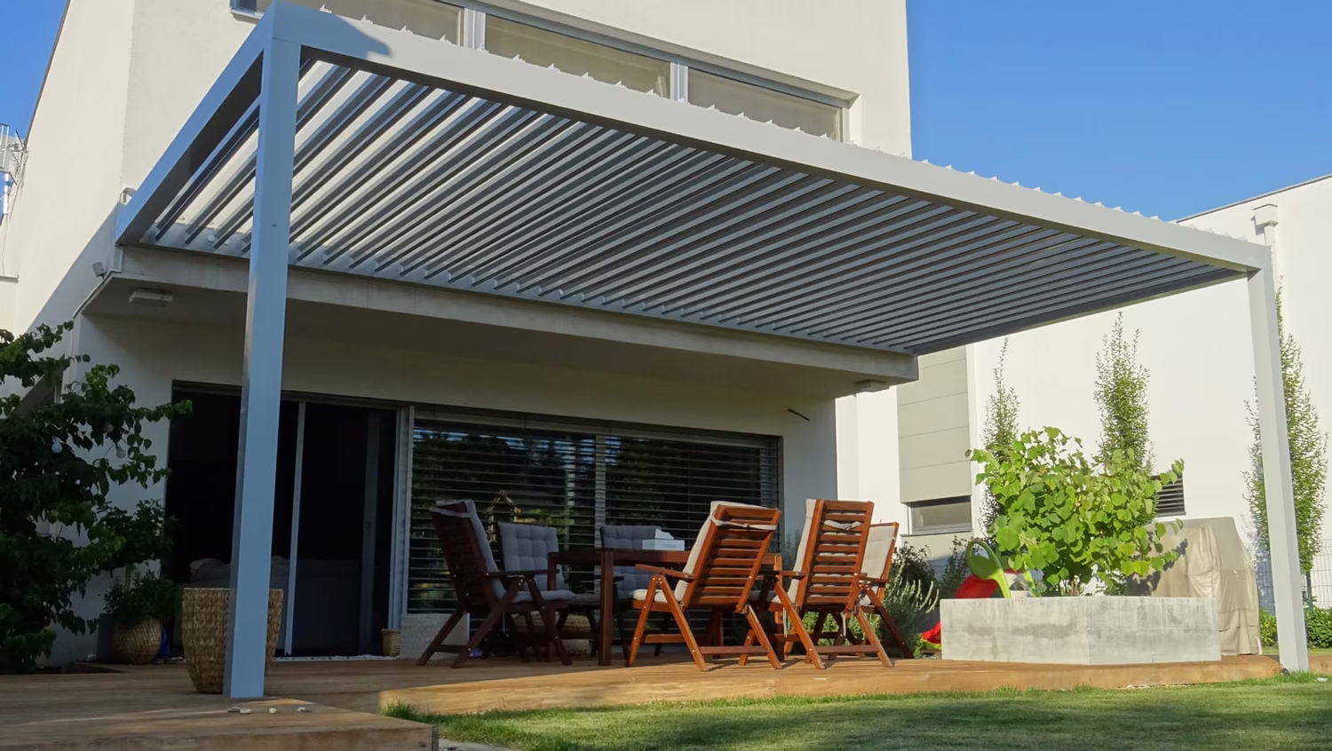 Bioclimatic aluminium pergola with adjustable louvres over a terrace with a dining set by a modern house