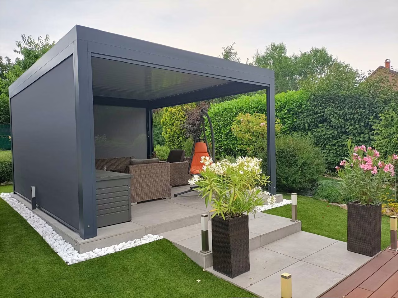 Anthracite bioclimatic aluminium pergola with a side screen and rattan seating in a garden