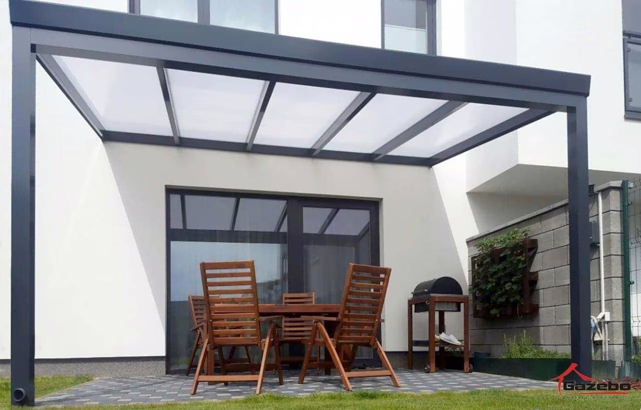 Anthracite Economic Class aluminium pergola beside a white house with a wooden table and chairs