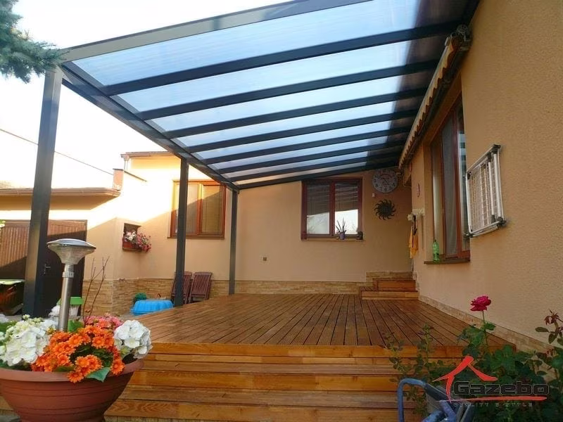 Anthracite Economic Class aluminium pergola over a wood deck with a patio heater and flowers