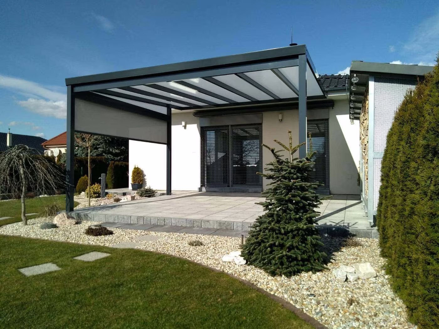 Anthracite Economic Class aluminium pergola beside a modern white house with a landscaped garden