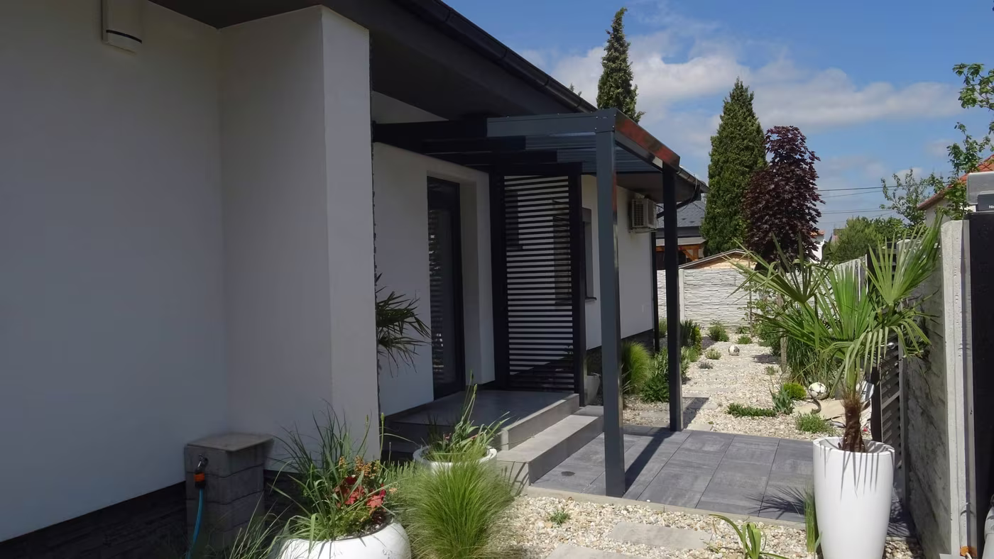 Anthracite Economic Class aluminium pergola running along a white house with potted plants