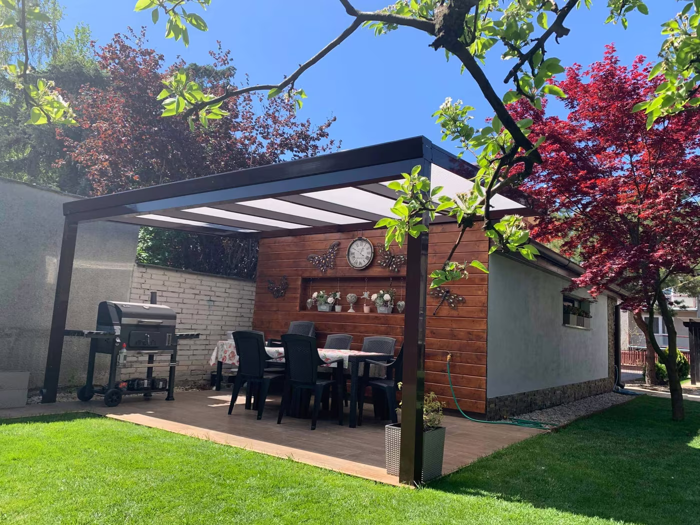 Anthracite Economic Class aluminium pergola over a paved terrace with a grill and seating
