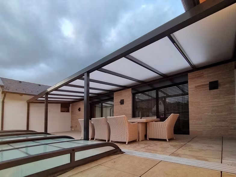 Anthracite Economic Class aluminium pergola over a pool enclosure with rattan seating