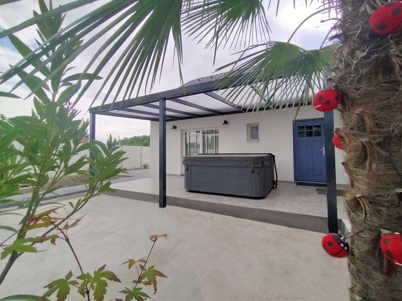 Anthracite Economic Class aluminium pergola with a hot tub and a palm beside a house