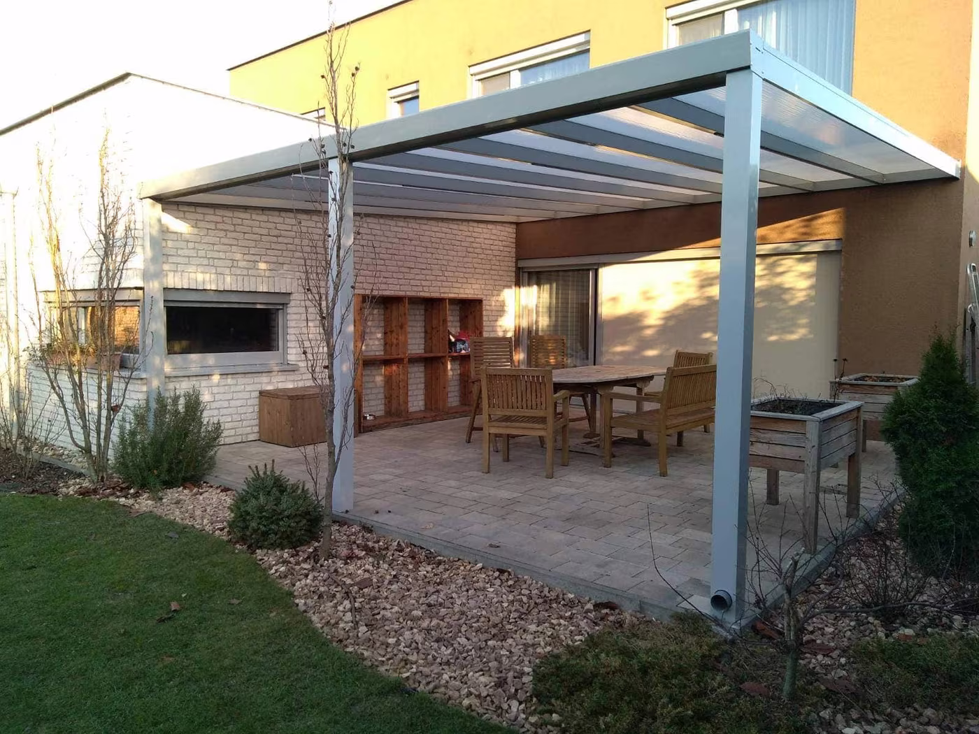 Silver Economic Class aluminium pergola over a gravel area with a dining set