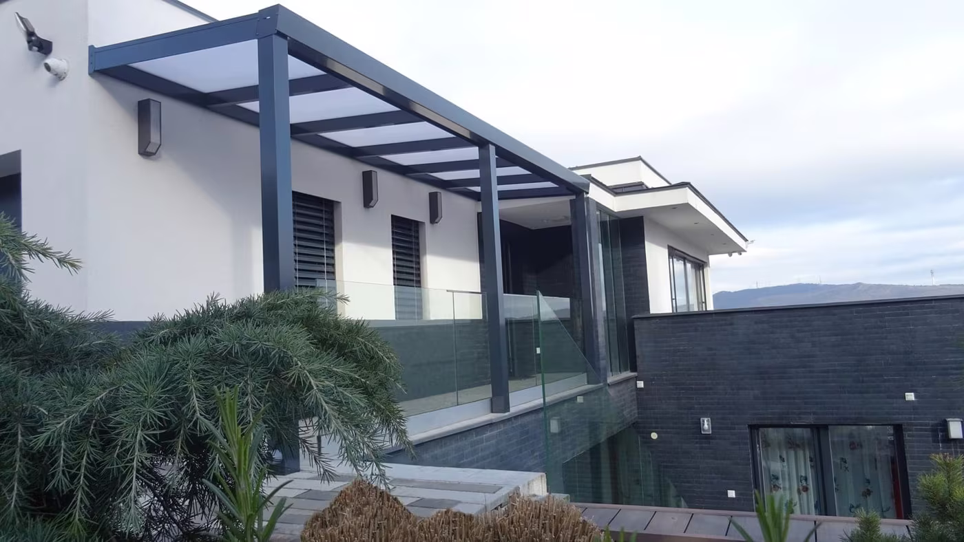 Anthracite Economic Class aluminium pergola beside a modern grey house with a glass balustrade