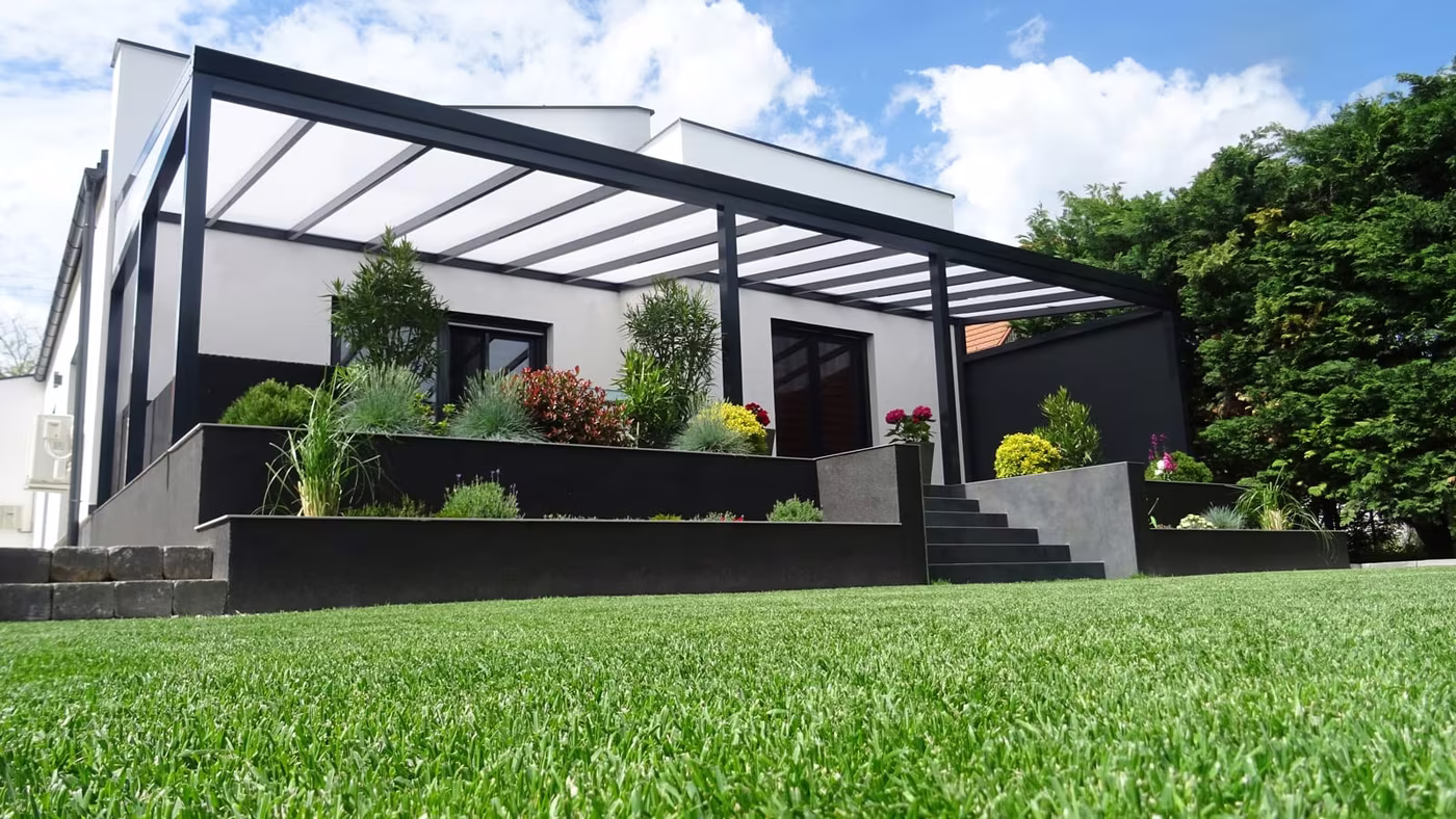 Anthracite Economic Class aluminium pergola over a terrace on a sloped plot with a lawn