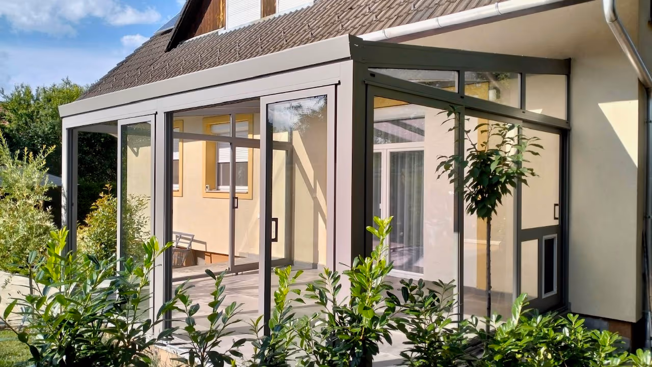Economic Garden winter garden with sliding glass doors beside a yellow house