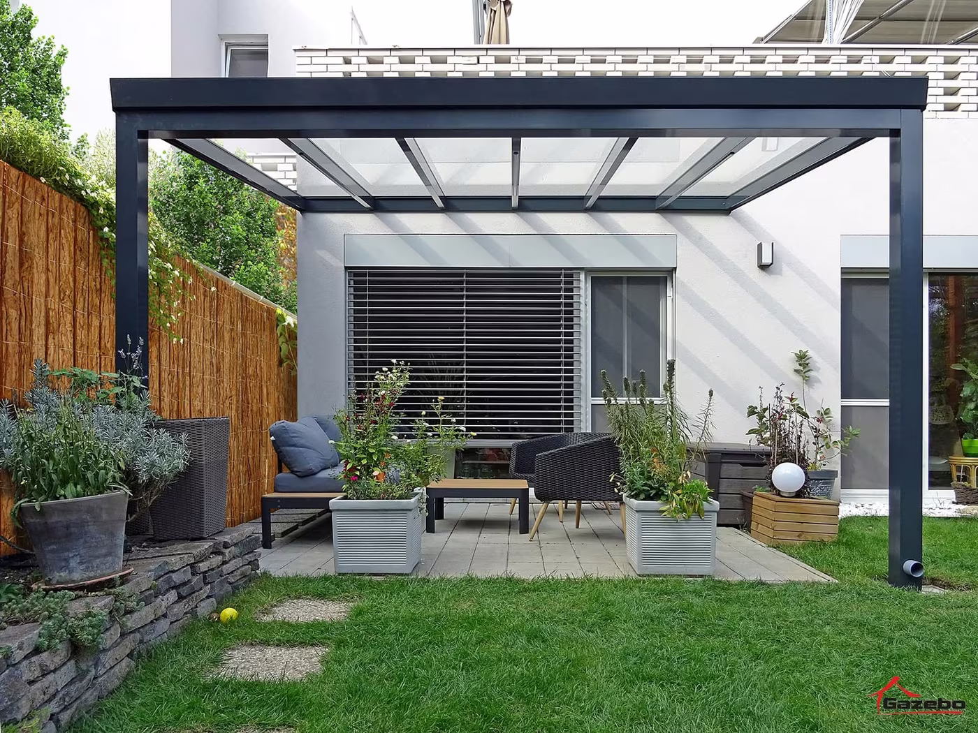 Anthracite Top Class aluminium pergola over a terrace with seating by a house with a wooden fence
