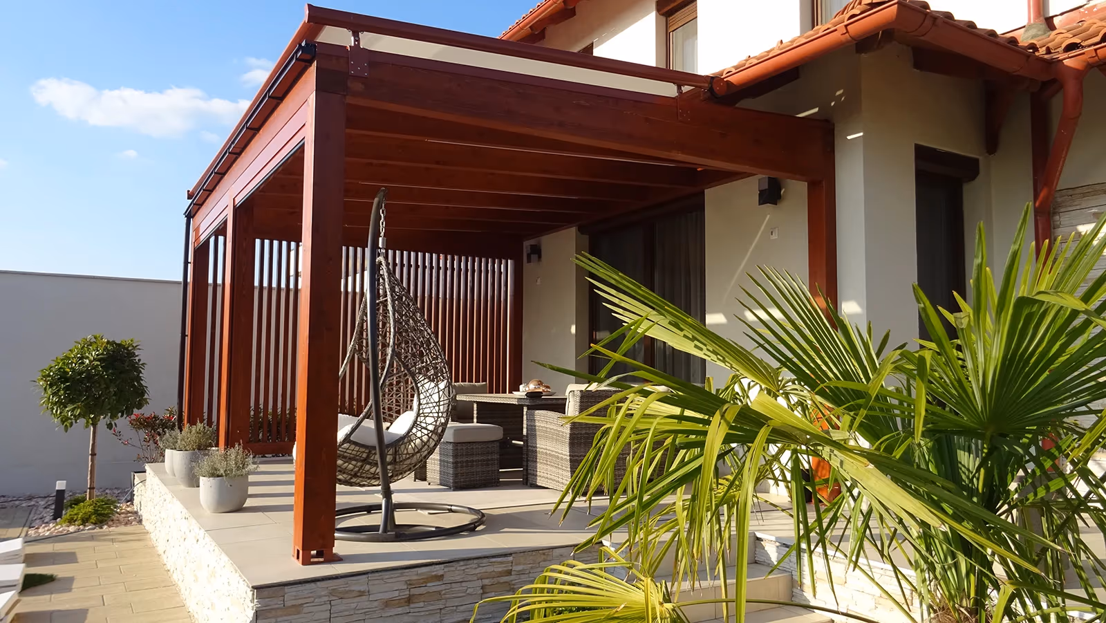Milano wooden pergola with a hanging chair and a palm tree