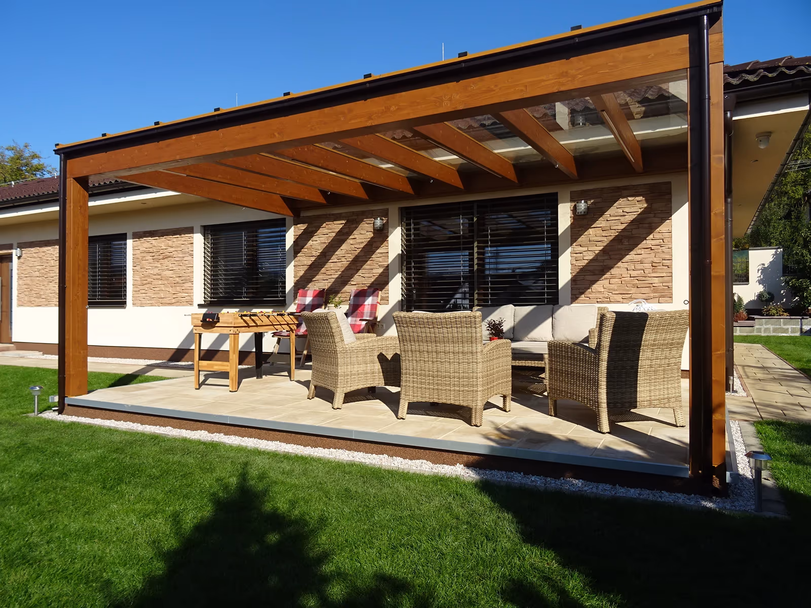 Milano wooden pergola with a dining set beside a stone house