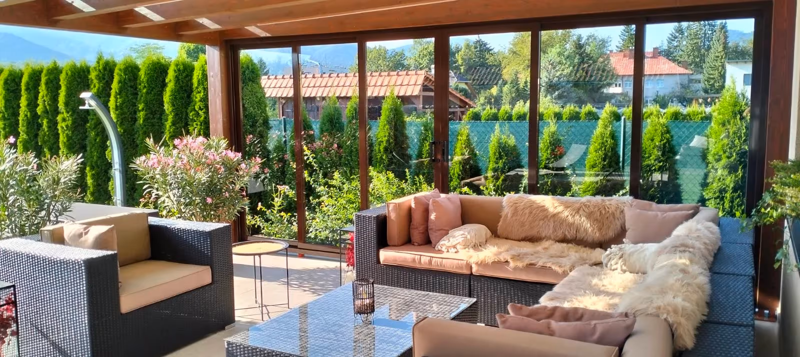Furnished Milano wooden pergola with a large sofa beside a house with a red tiled roof
