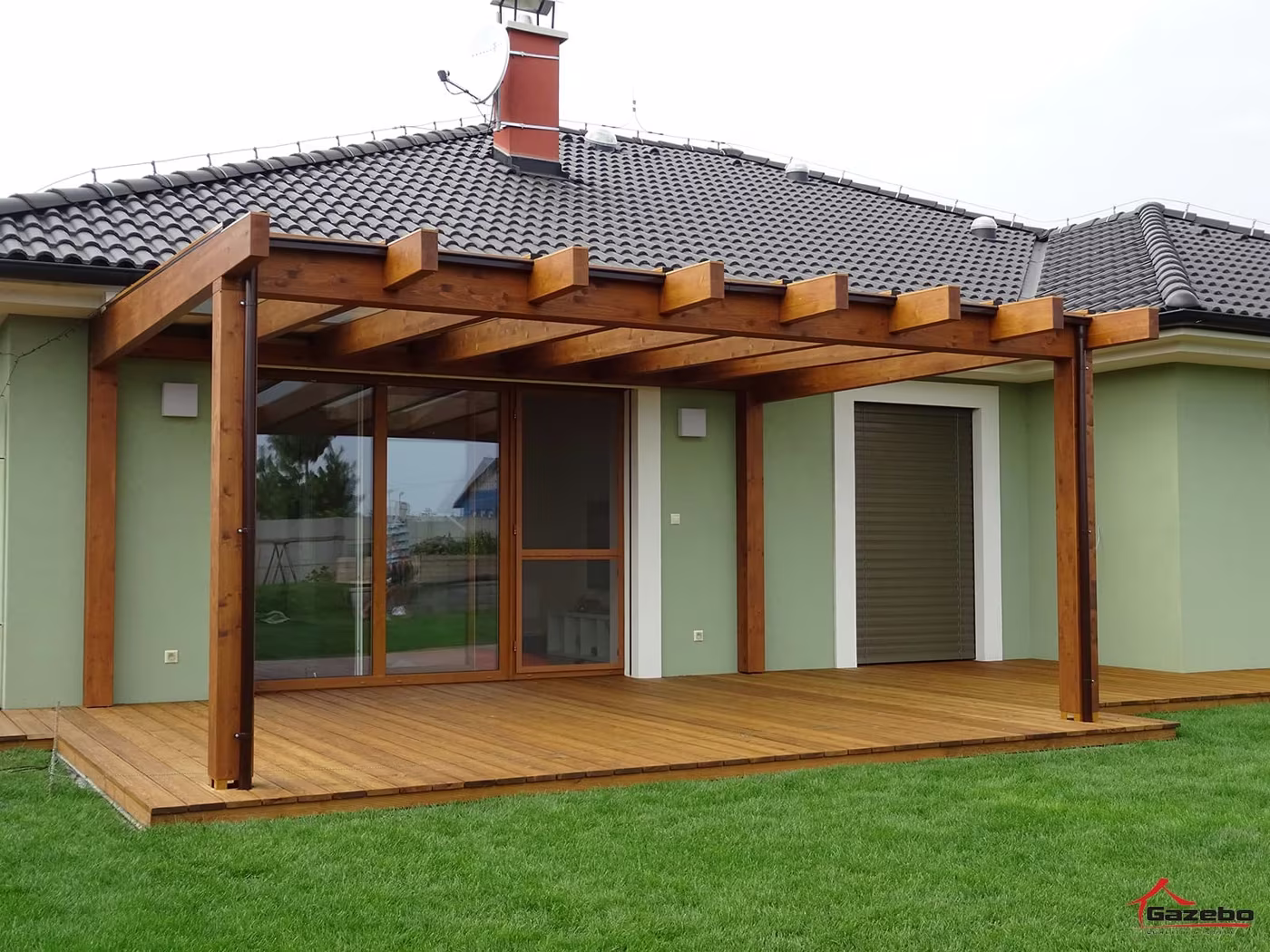 Fenix wooden pergola by a house with glazed doors over a wood deck with a lawn
